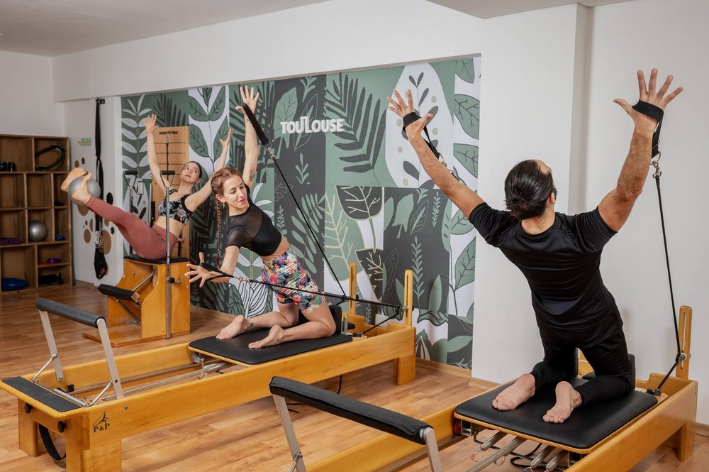 Clase grupal en Toulouse Pilates: tres personas entrenando sobre Reformer y Chair