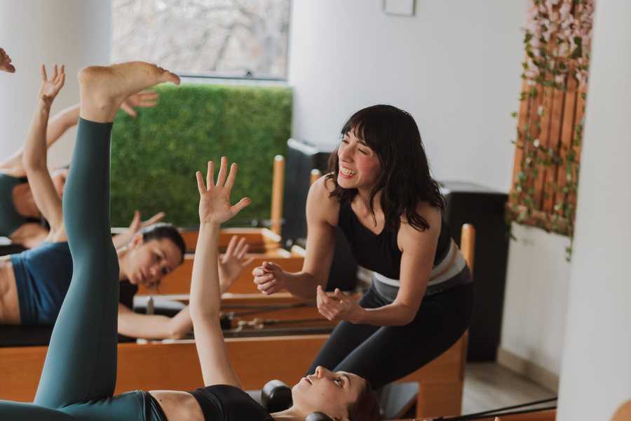 Clase de Pilates en dúo: dos personas entrenando con una profe acompañando